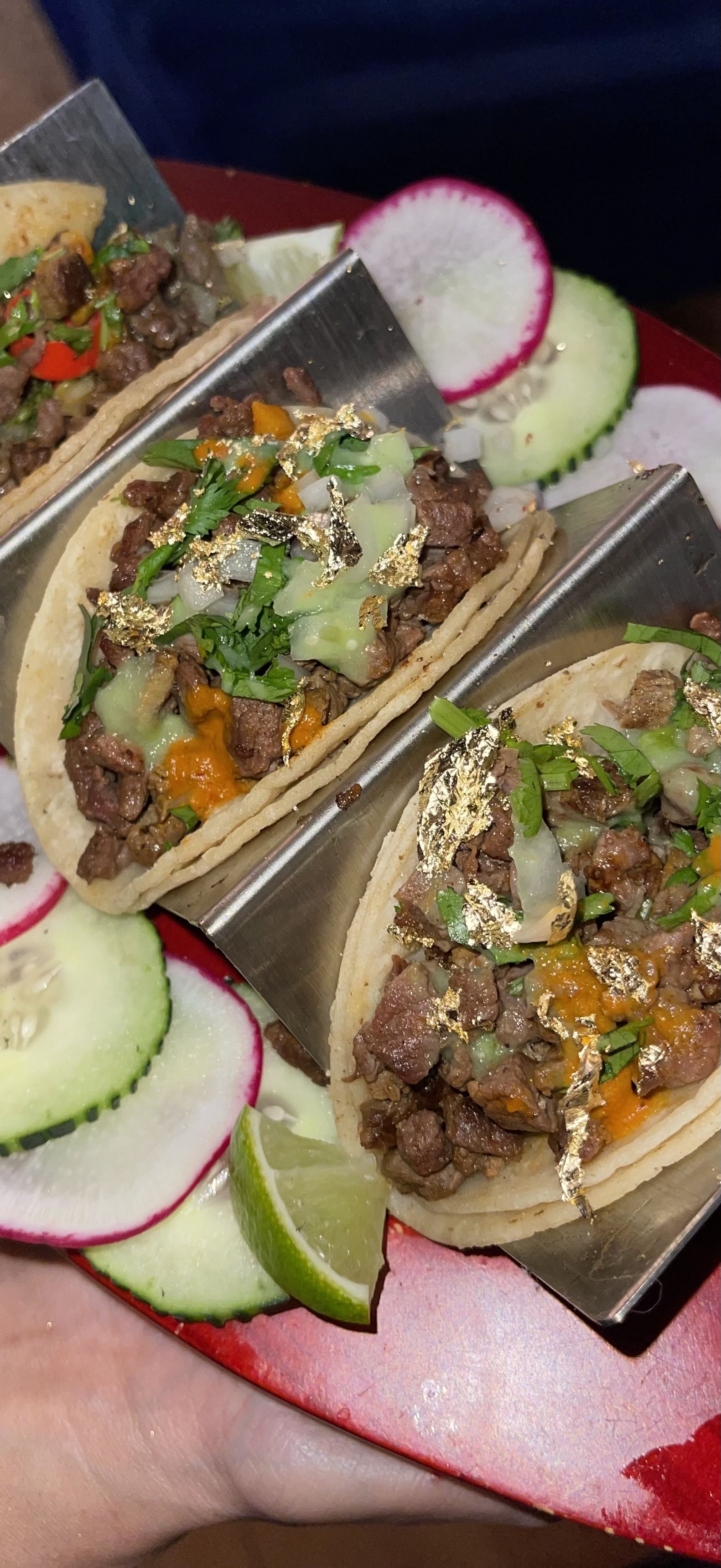 Gold leaf tacos served on stainless taco holders with radish, cucumber and lime