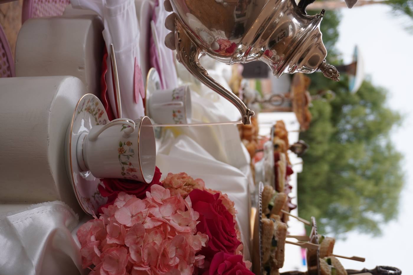 Silver teapot pouring into china cup with pink hydrangeas